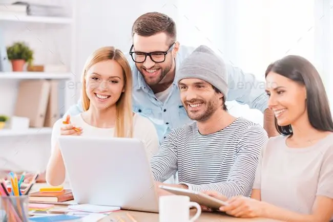 Grupo de cuatro personas sonrientes reunidas alrededor de una laptop, colaborando en un espacio de trabajo.